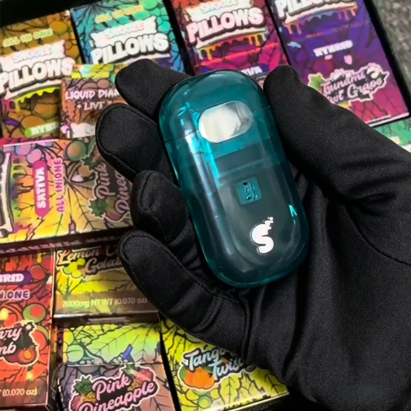 Gloved hand holding a teal Snooze Pillows 2g empty vape cart device over packaging.