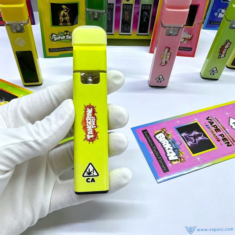 Handholding a yellow empty Sluggers Hit 1ml disposable vape device with Tangerine Twist strain print.